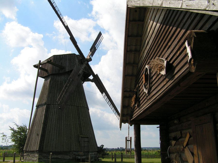 Historische Holzwindmühle und ein traditionelles Holzgebäude im Freilichtmuseum Dudutki in Belarus