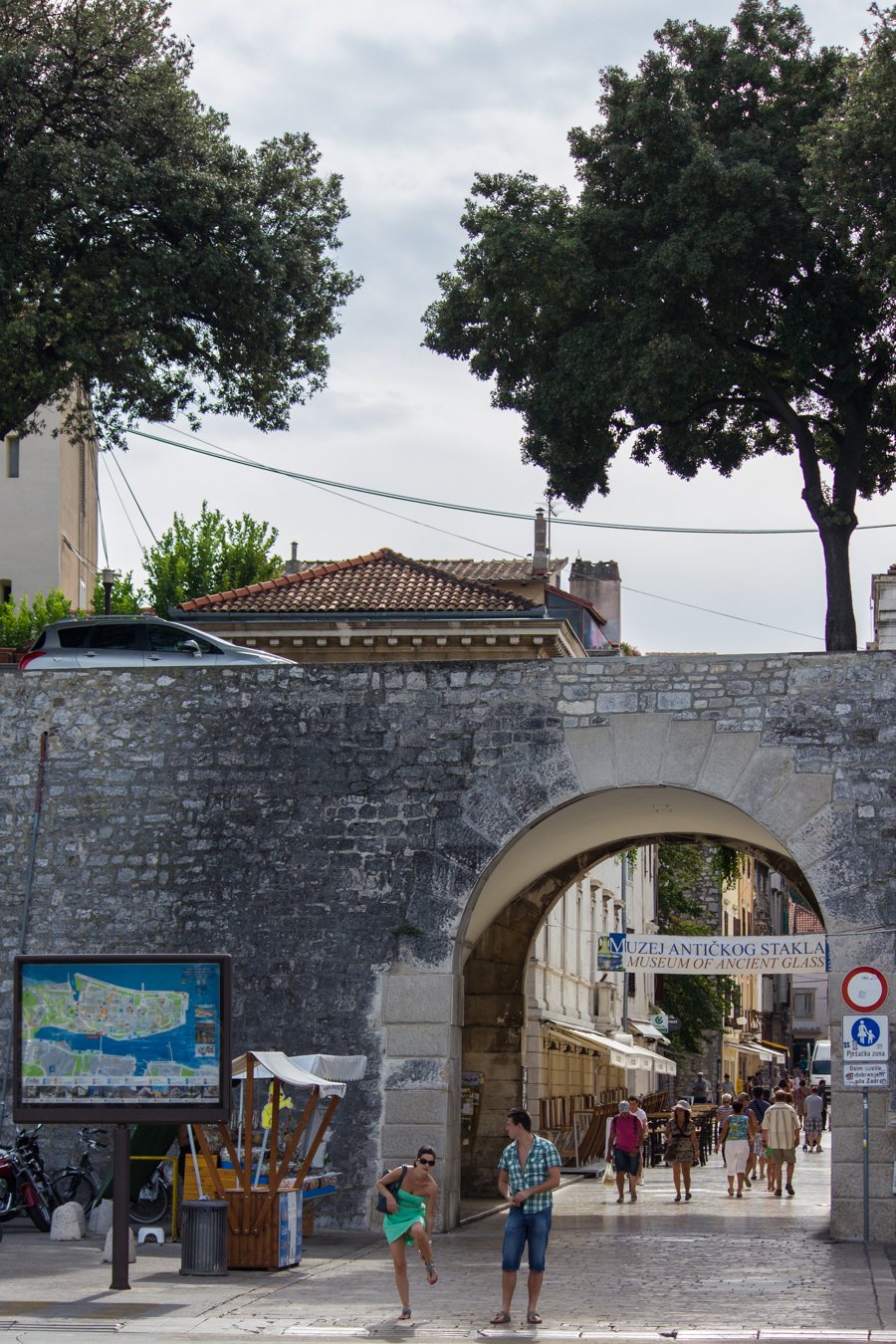 Steinbogen führt in eine Altstadtstraße mit Fußgängern und Museumsschild